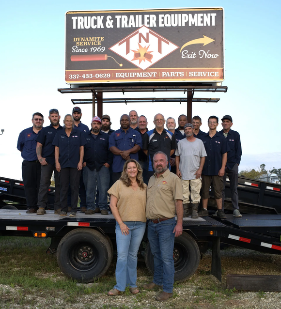 Truck and Trailer Equipment staff pose on a trailer in front of their business sign.