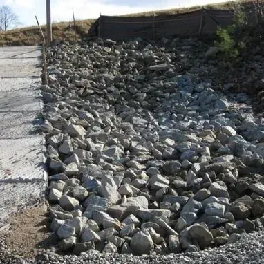 Gravel and rocks border a concrete path next to a hill, used for erosion control.