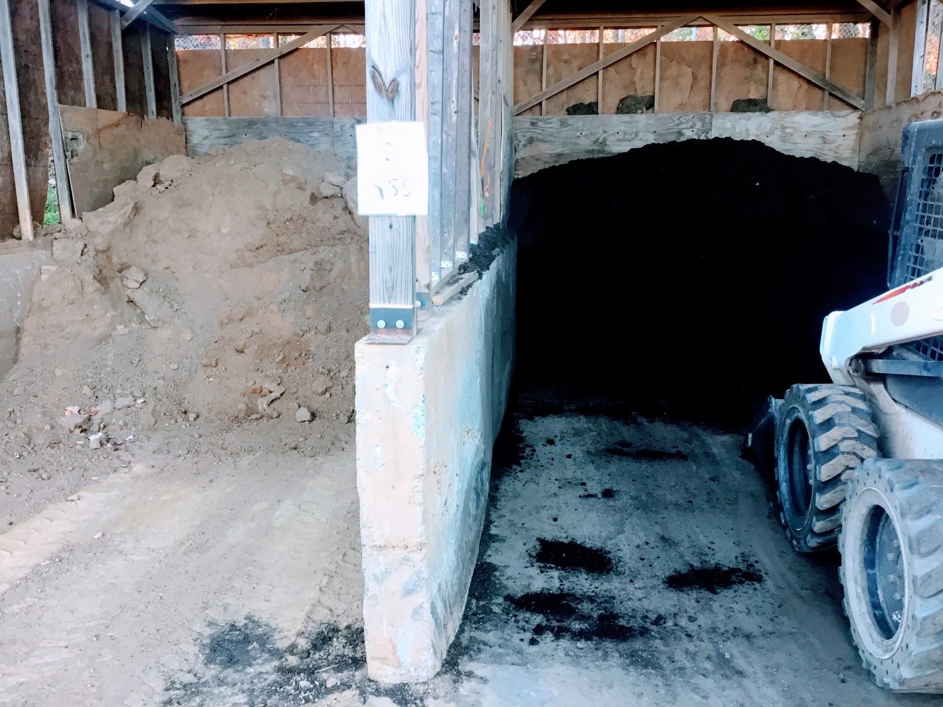 A small loader near a dark mound of material in a shed. Light-colored mound on left.