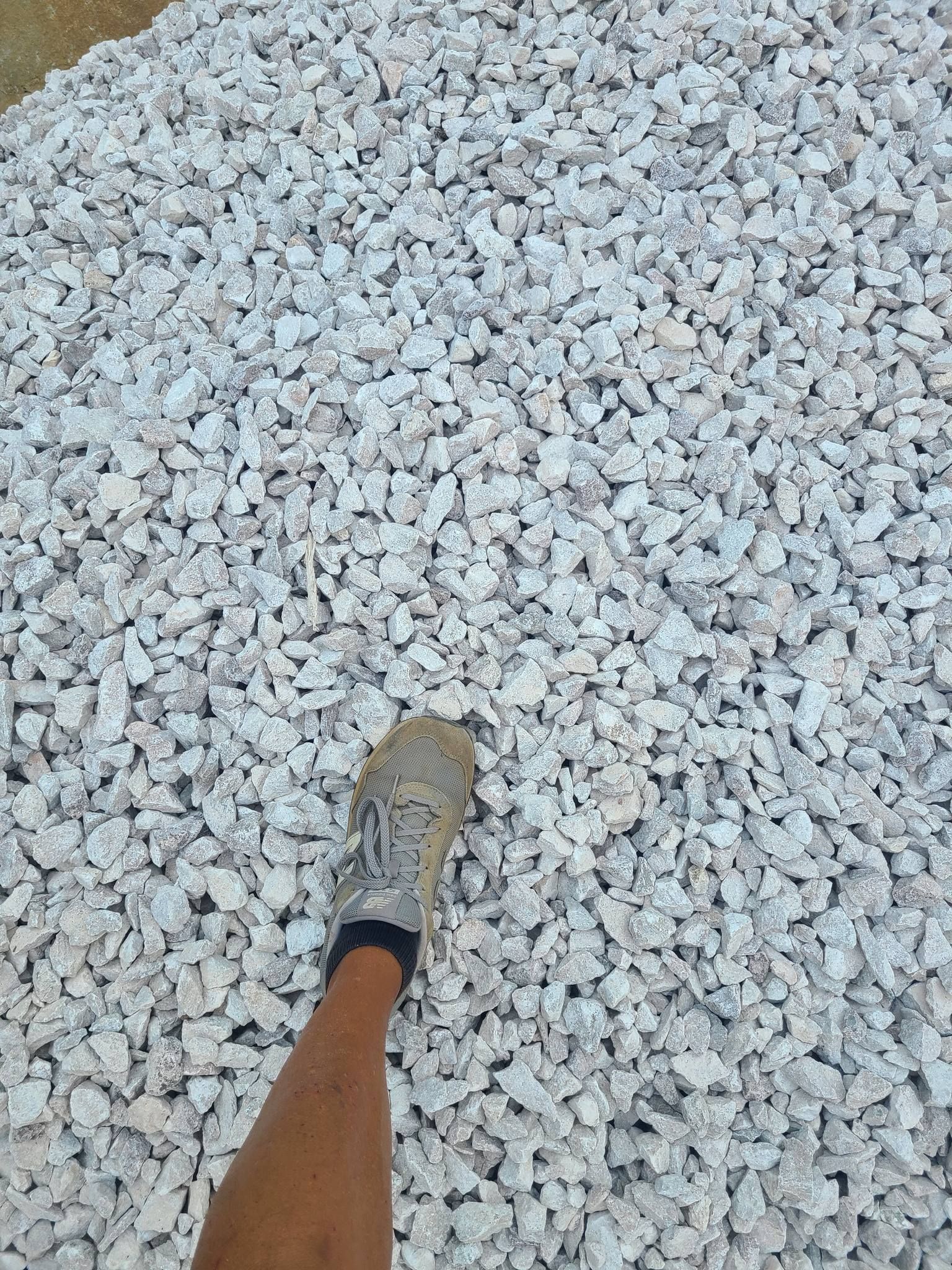 Foot in a dirty sneaker on a pile of white gravel.