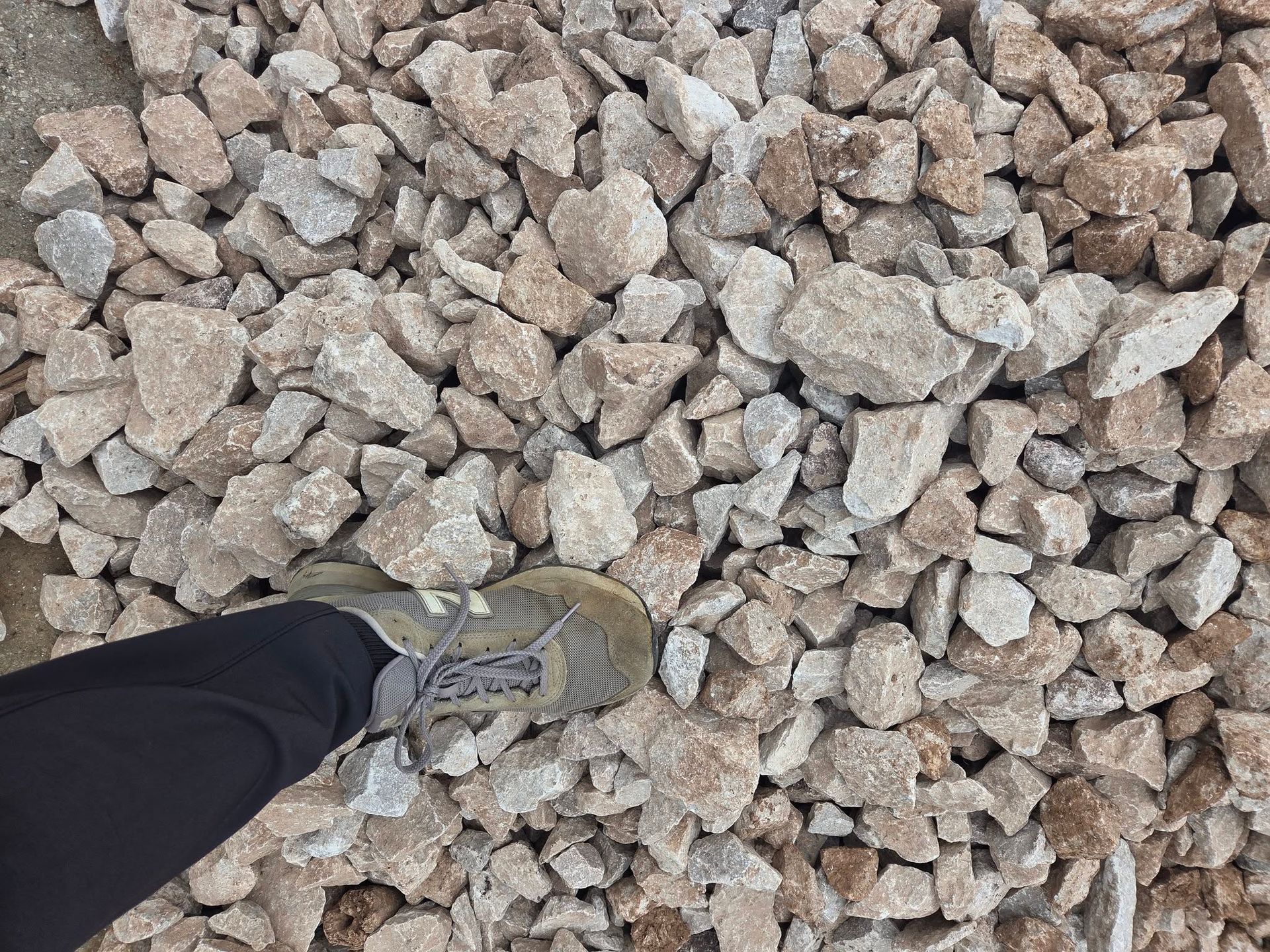 Foot wearing a tan shoe steps on a bed of tan and gray gravel.