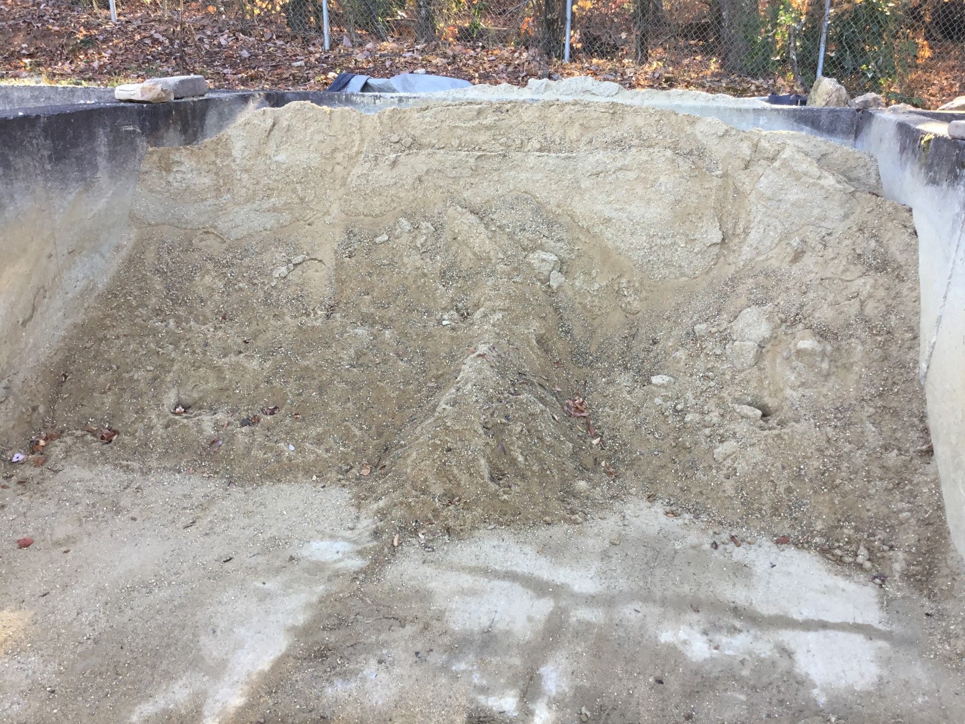 Pile of light brown sand within concrete retaining walls, outdoors.