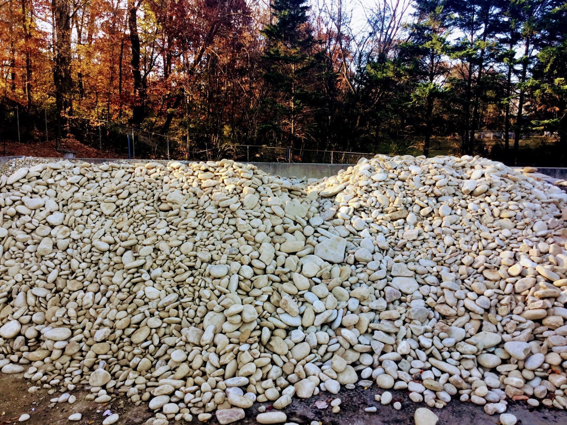Two large piles of light-colored, smooth stones; trees in background.