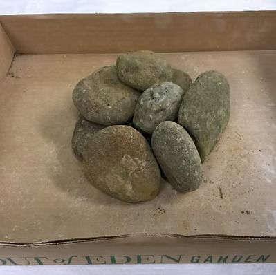 Smooth, tan river rocks piled in a brown cardboard box.