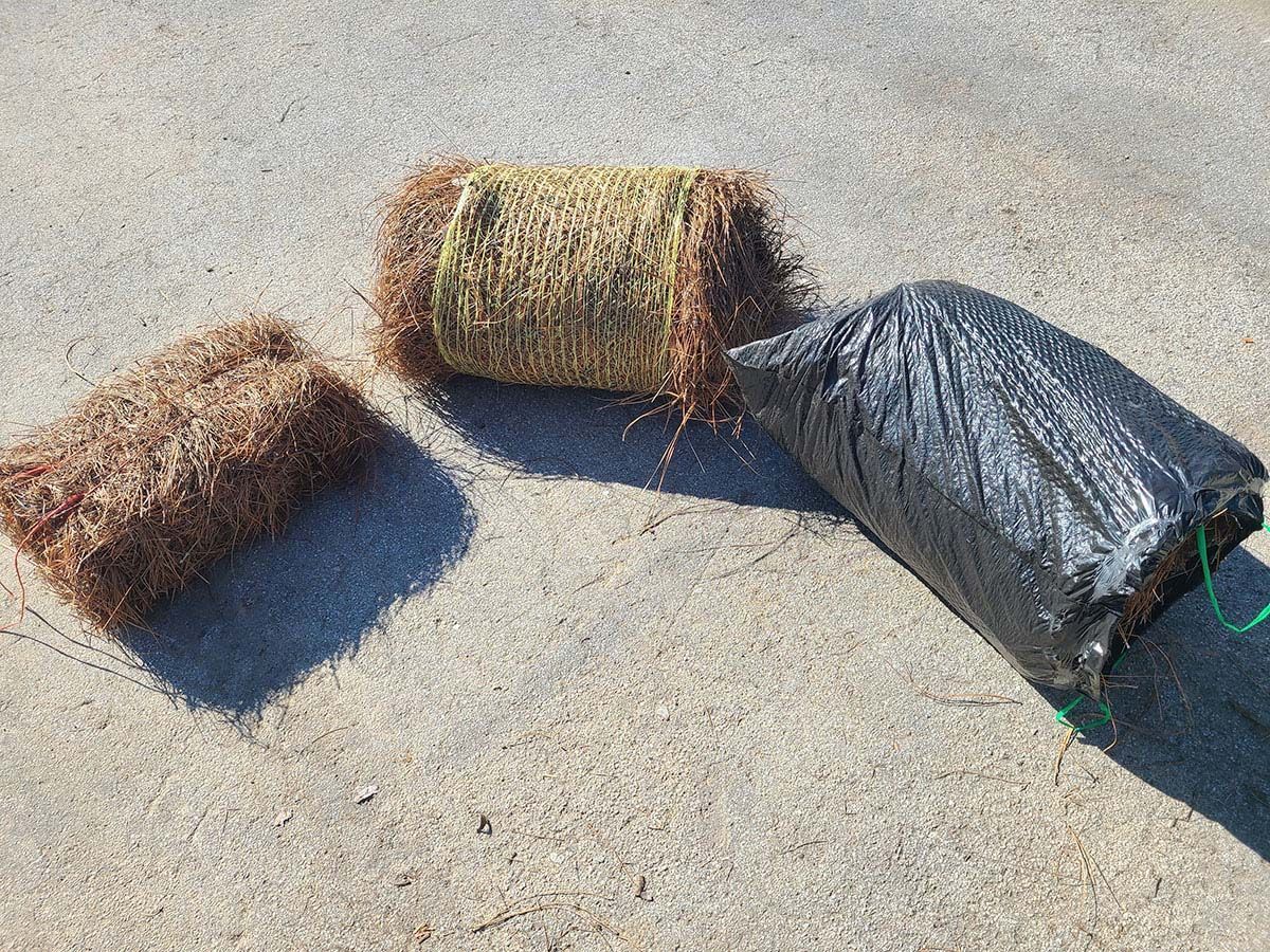 Three rolls of brown erosion control material on concrete. One is in a black mesh bag.