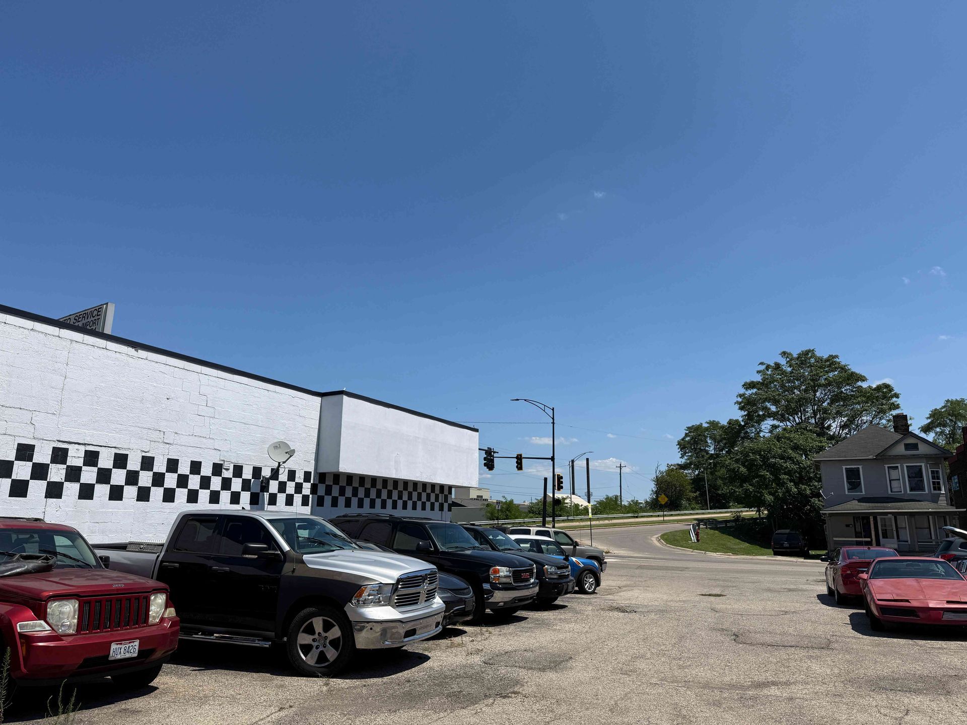 Parking lot beside a white building with black checkered trim, several parked cars, and a clear blue sky