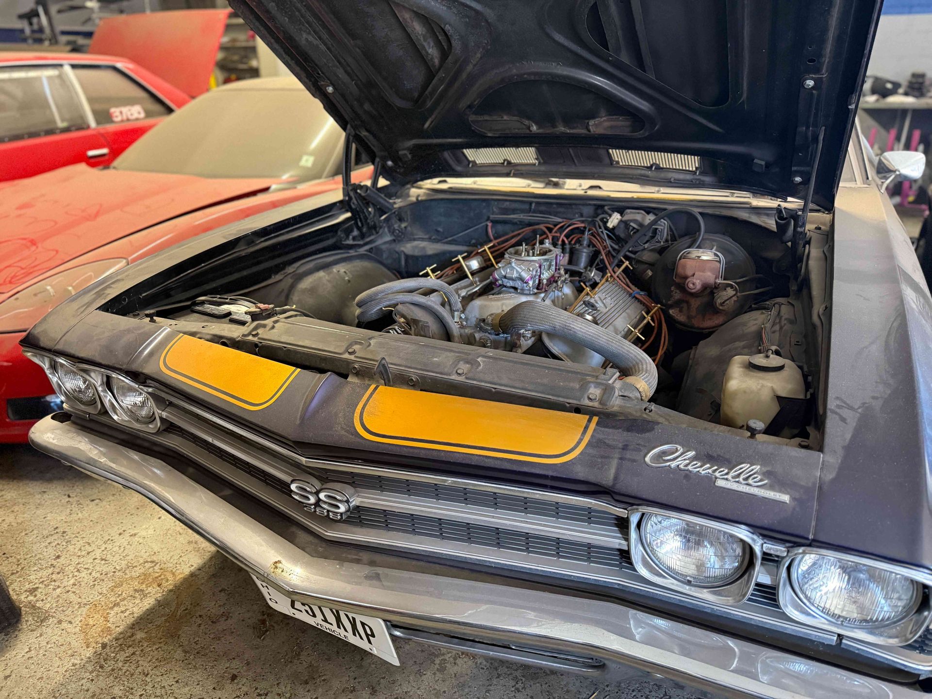 Classic black muscle car with hood open, exposing the engine in a garage or car show setting.