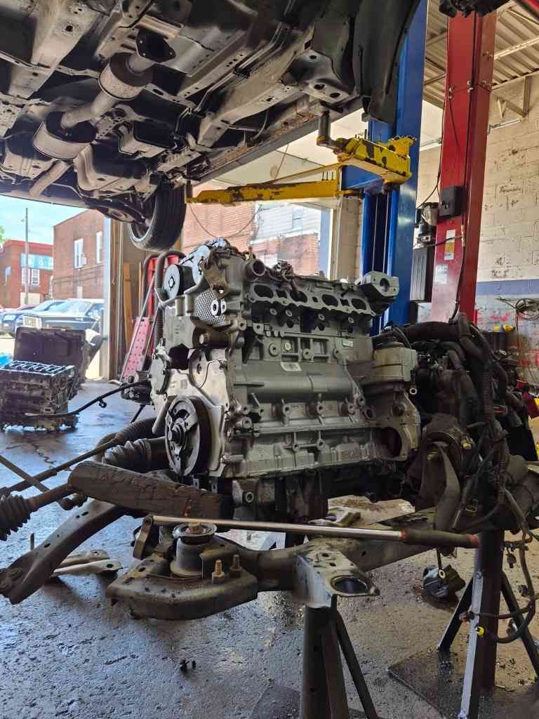 Car engine removed in an auto repair shop, suspended on a lift with tools and parts nearby