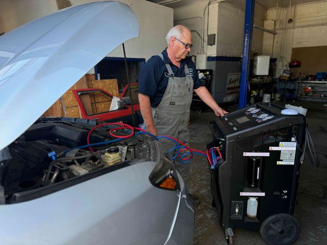 Mechanic in a garage checking equipment beside an open car hood and a black cart on wheels