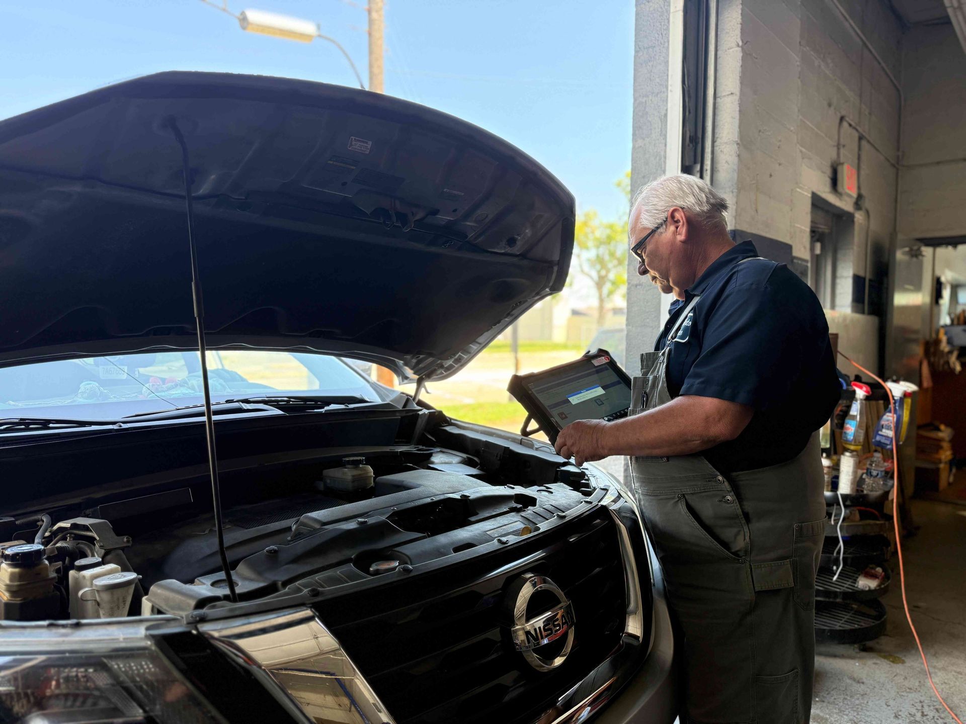 Mechanic inspecting a black car with hood open in a garage bay