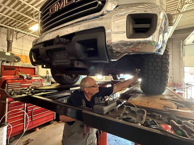 Mechanic working under a lifted truck in an auto shop, with tools and red tool chests nearby
