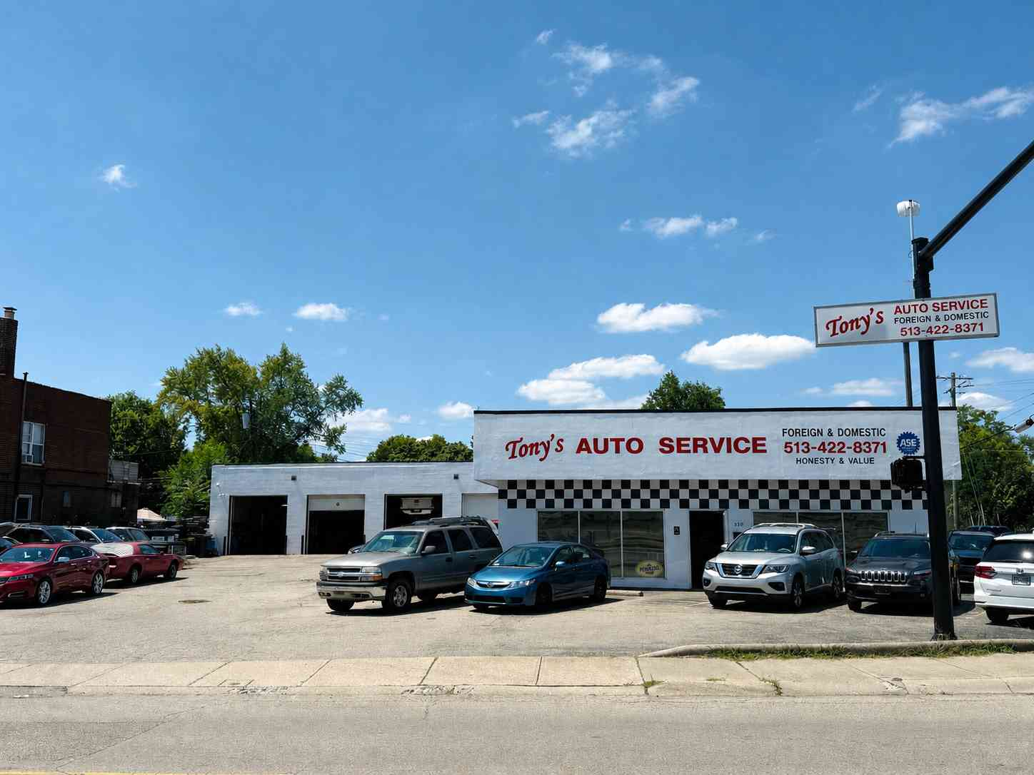 Auto service shop with parked cars, white building, and roadside sign on a sunny day