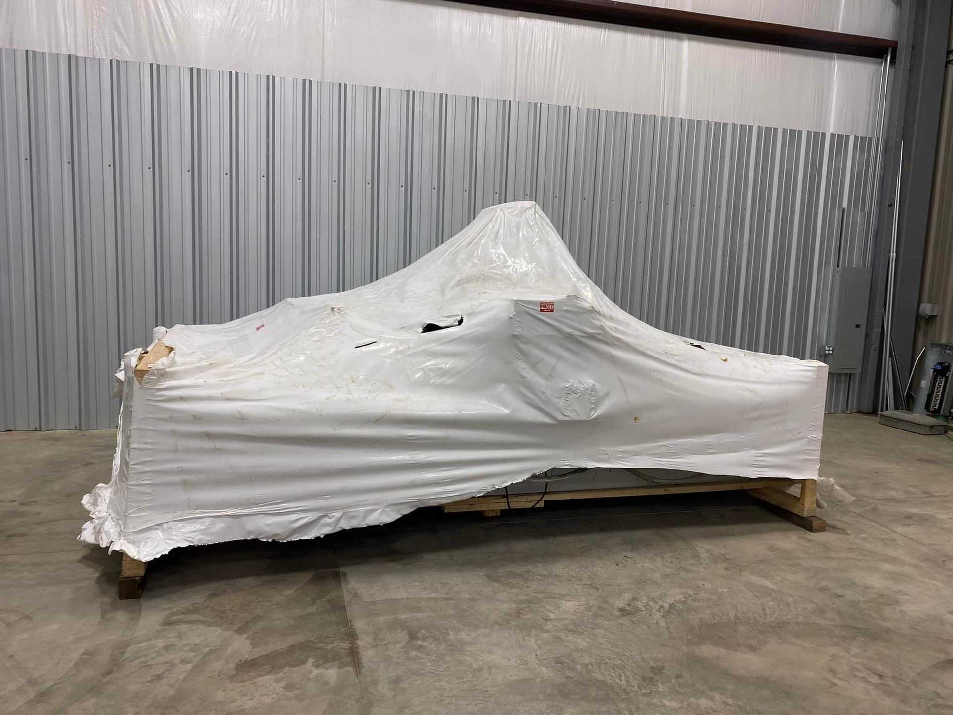 A motorcycle is wrapped in plastic and sitting on a wooden crate in a warehouse.