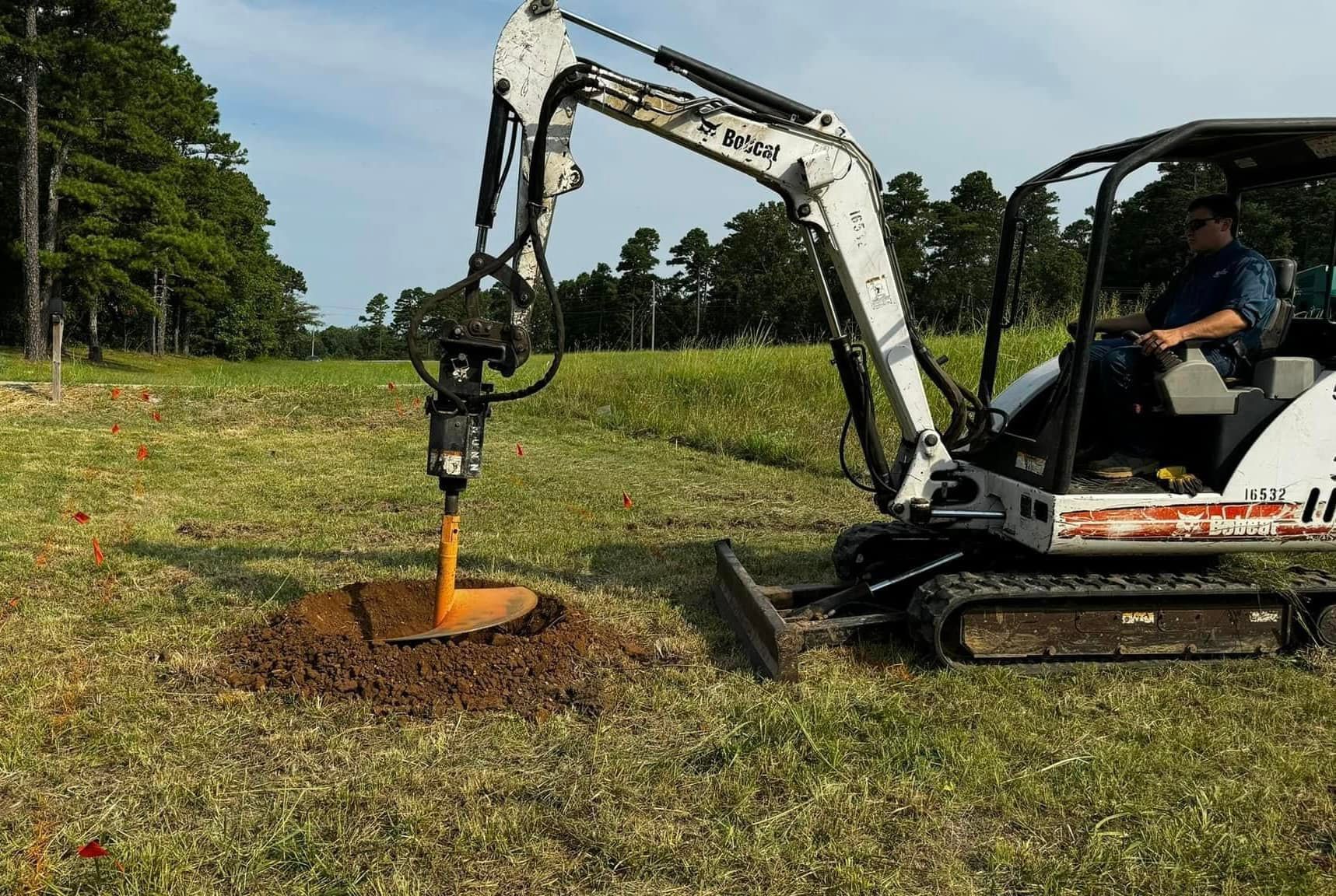 A man is driving a small excavator in a grassy field.