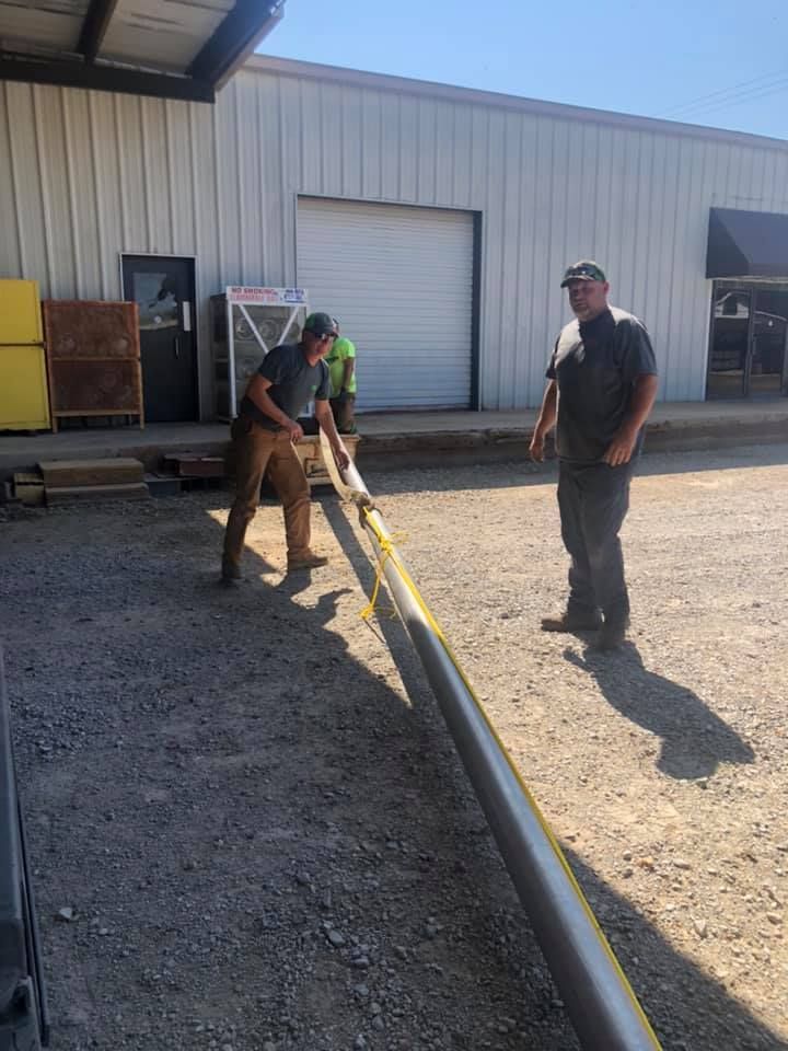 Two men are measuring a pipe in a parking lot.