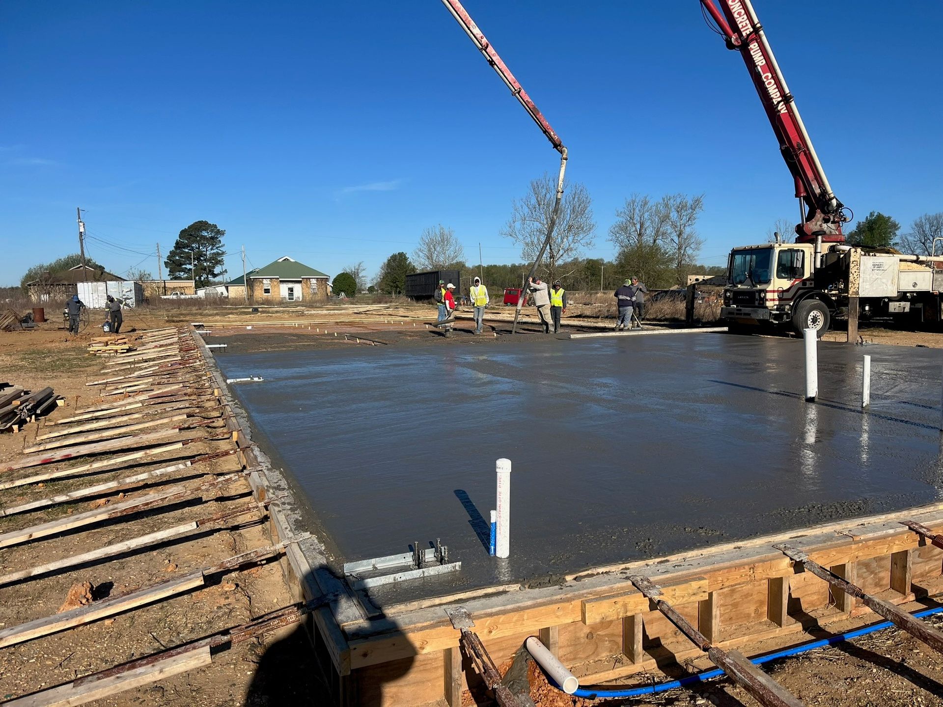 Construction site with concrete being poured for a foundation. Workers and a concrete pump truck are visible.