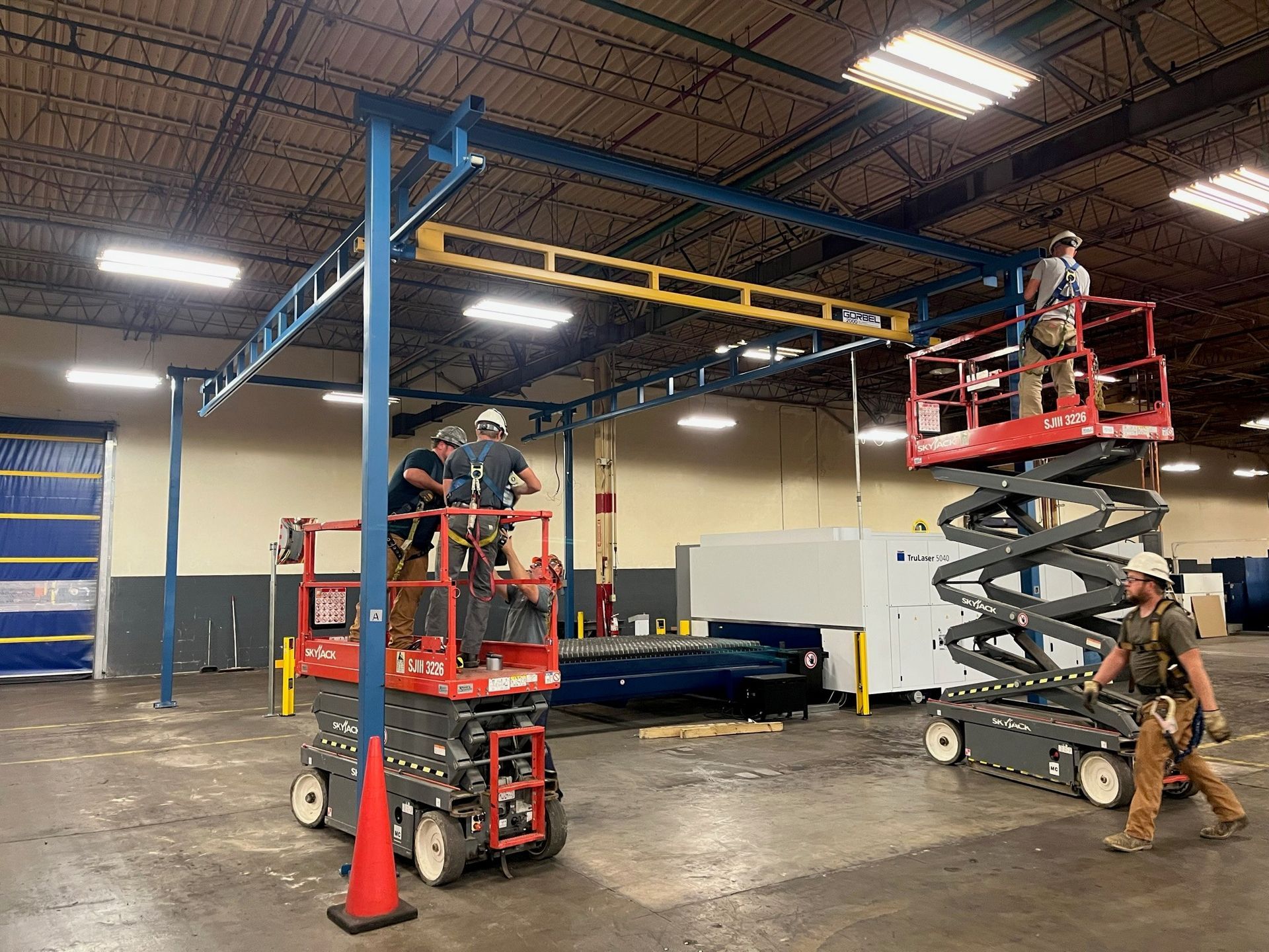 Workers on scissor lifts installing overhead steel frame in warehouse.