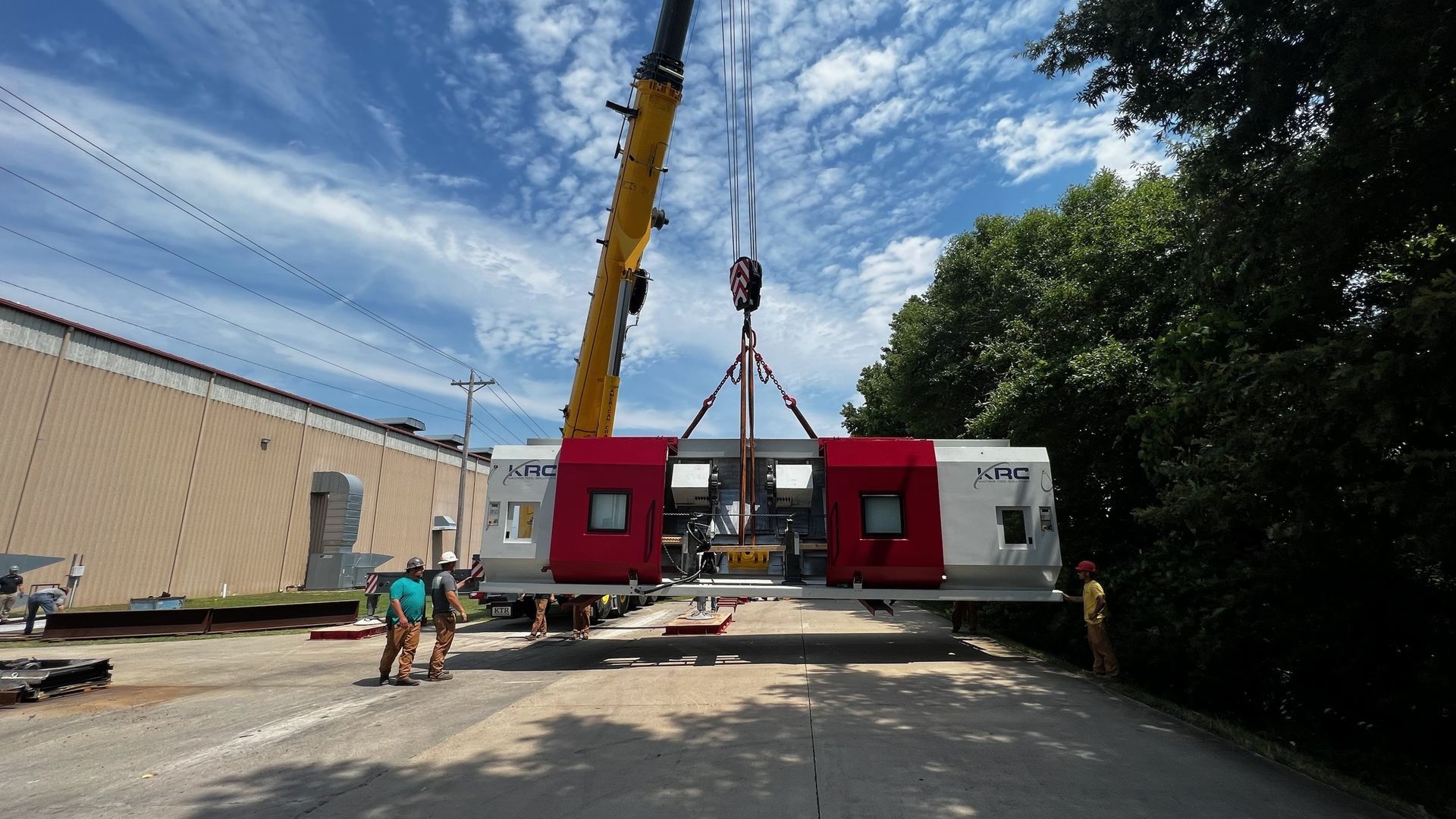 A crane lifting a modular building section with red doors on a road; workers nearby.