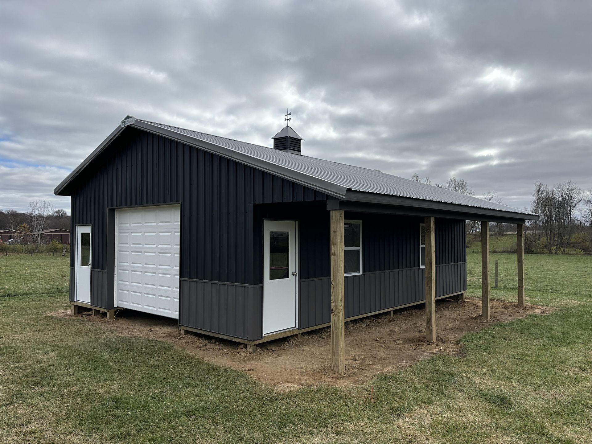 A black and white garage with a porch in a field.
