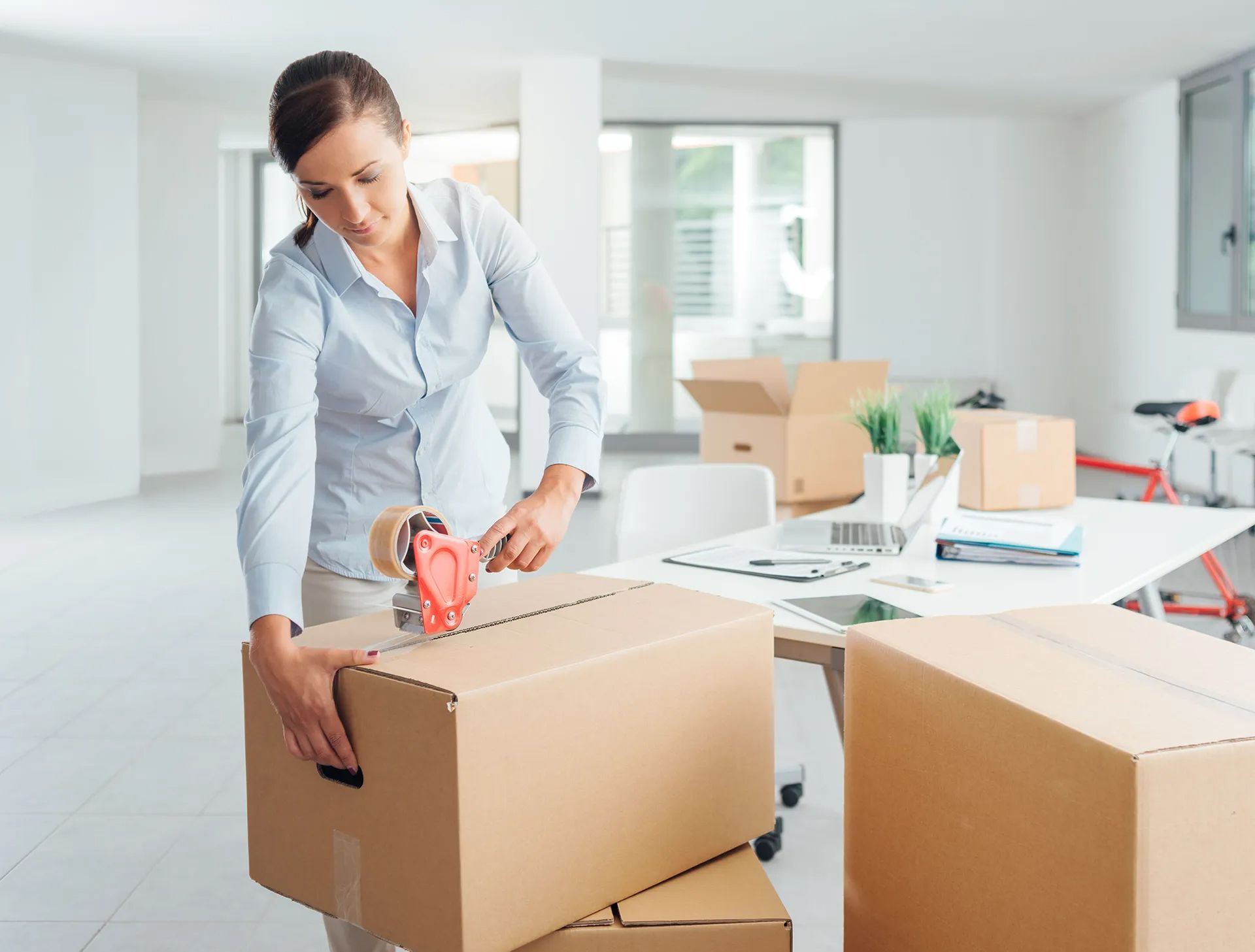 Person sealing cardboard boxes in a bright office during a move