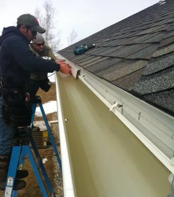 Two people install a gutter on a roof, using tools.