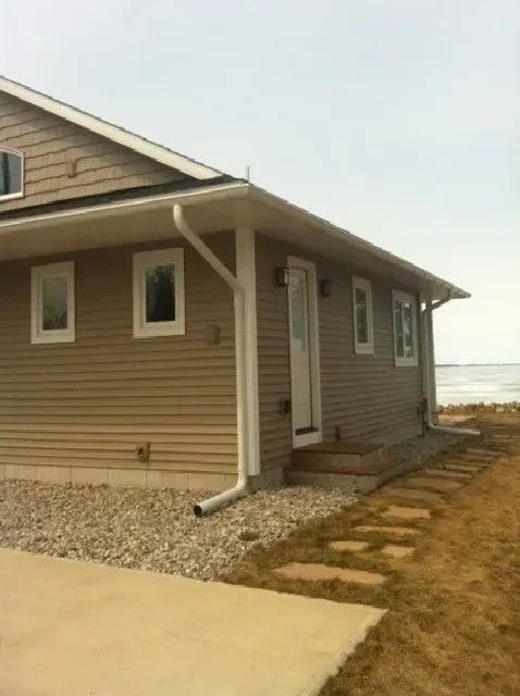 Beige house with white trim, small windows, and a paved path leading to a door.