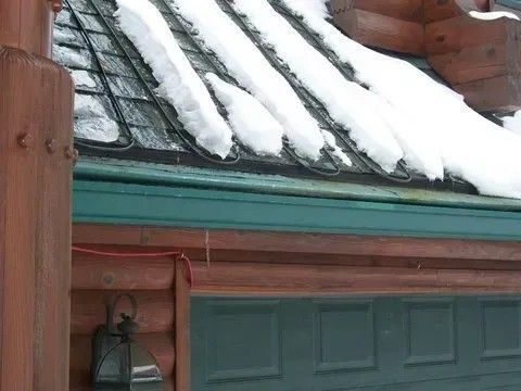 Snow-covered roof of a log cabin with a teal-colored garage door and trim.