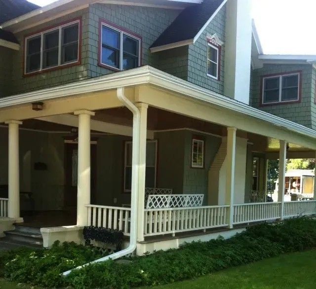 Green two-story house with a wraparound porch; white pillars, trim, and railing.