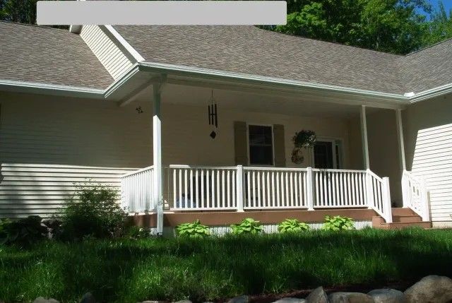 Beige house with a white porch railing, brown deck, and green lawn.