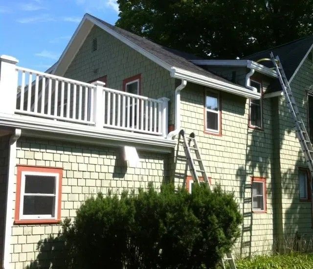 Green house with white deck, ladders, and gutters. Windows have red trim.