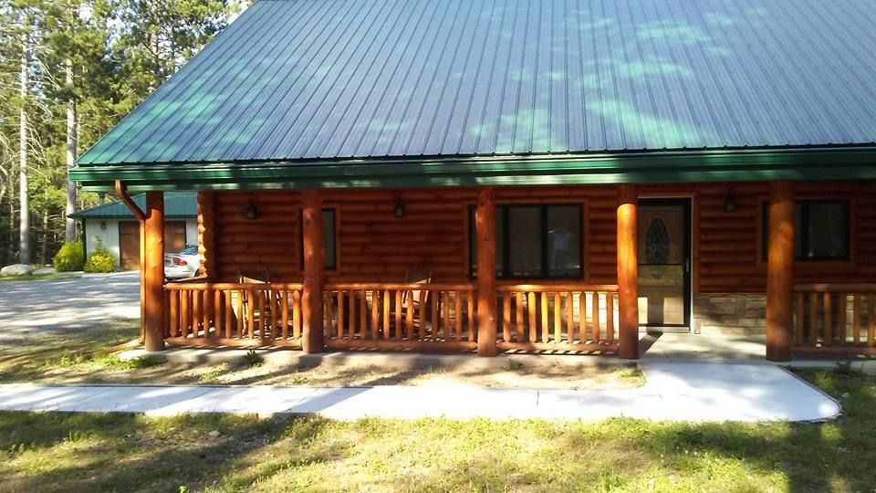 Log cabin with green metal roof, front porch, and surrounding trees.