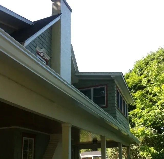 Green house exterior with white trim, porch, chimney, and trees.