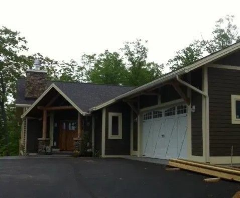 Brown house with white garage door and wooden accents; dark roof and chimney.