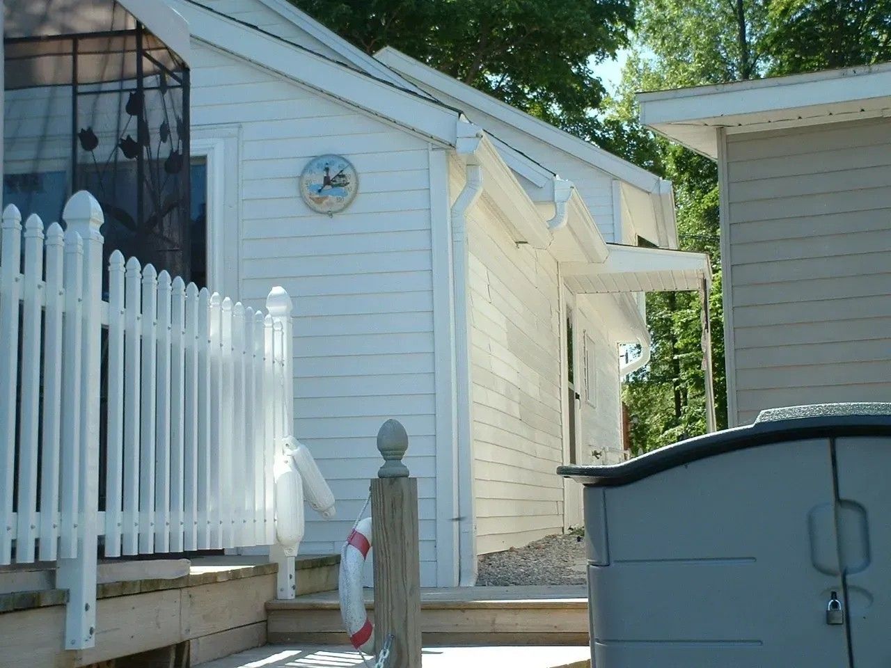 White building with picket fence, stairs, and a dark storage bin.