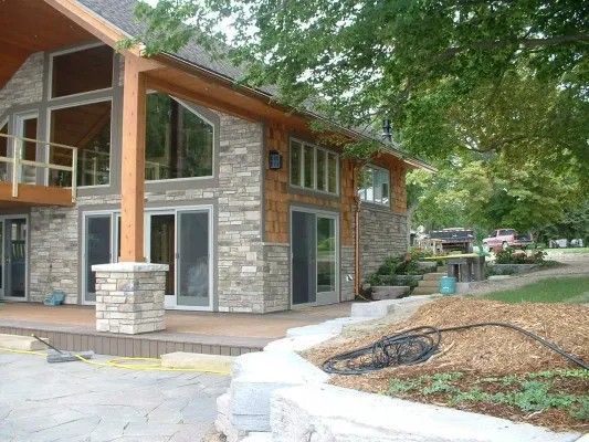 Stone and wood home with large windows, patio, and landscaped yard.