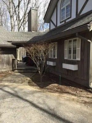 Brown building with white trim and shutters, leafless tree in front, paved driveway.