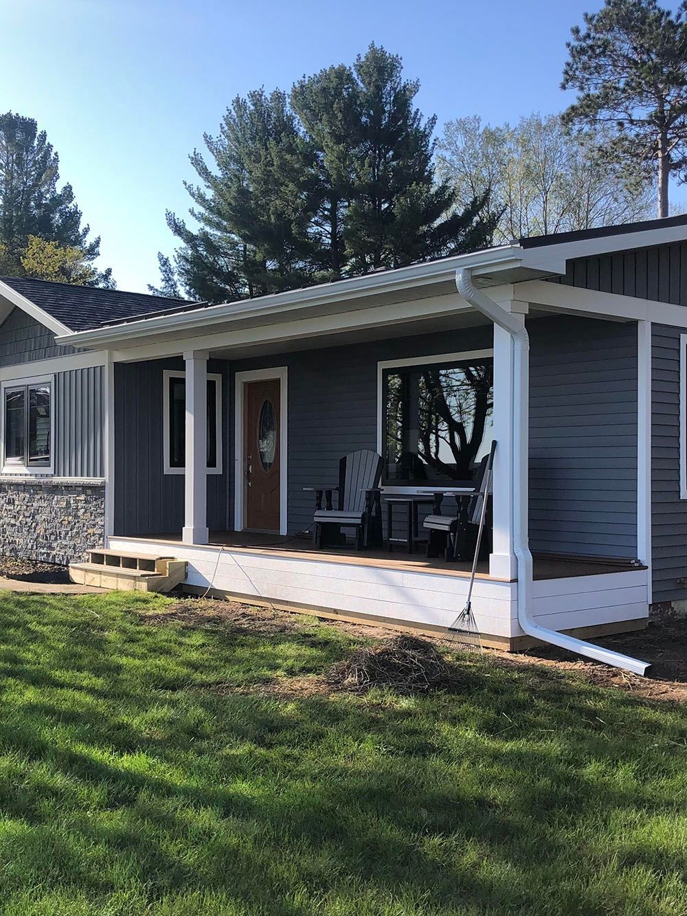 Blue-gray house with a white porch and pillars. A brown door and outdoor furniture are visible.