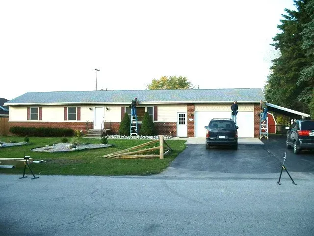 House with workers on ladders; cream siding, brick facade, black asphalt driveway.