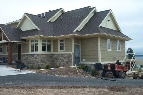 Beige house with stone and siding, a dark roof, and a small construction vehicle in front.