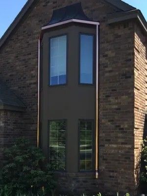 Bay window with copper trim on a brick house. Dark brown wall contrasts with the copper.