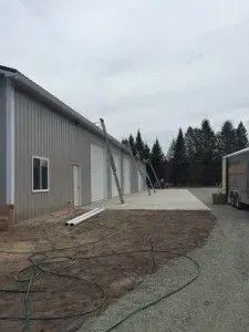 Gray metal building with concrete pad, supported by angled poles. Overcast sky.