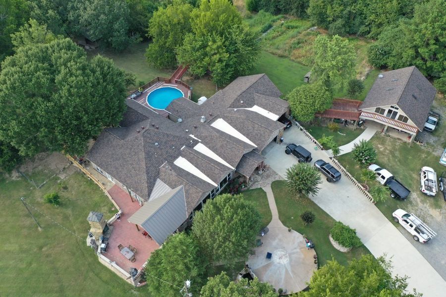 Aerial view of a large house with a pool and a long driveway, surrounded by trees.