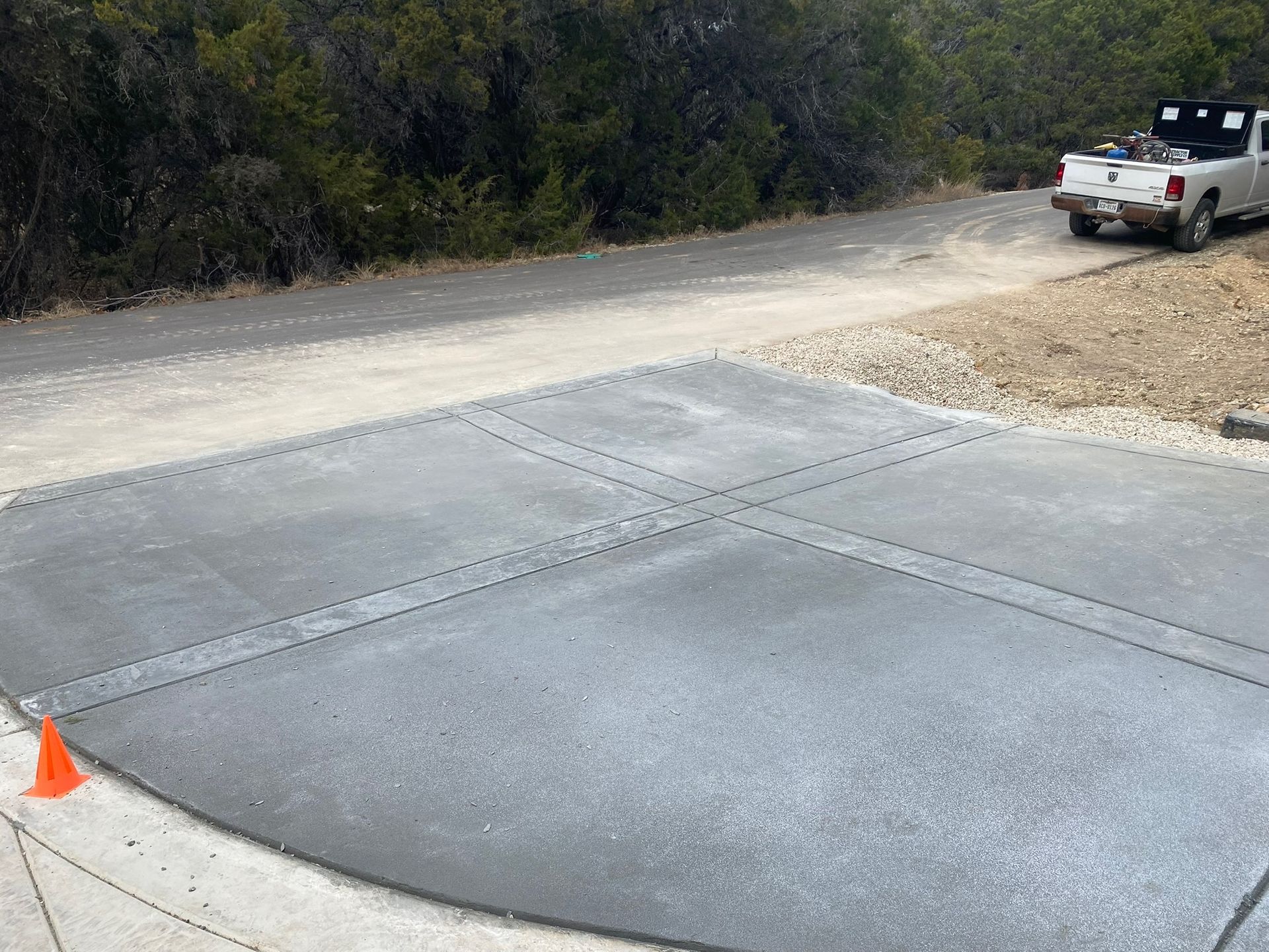 A freshly poured concrete driveway section with decorative patterned borders, adjacent to a dirt road and a white truck.
