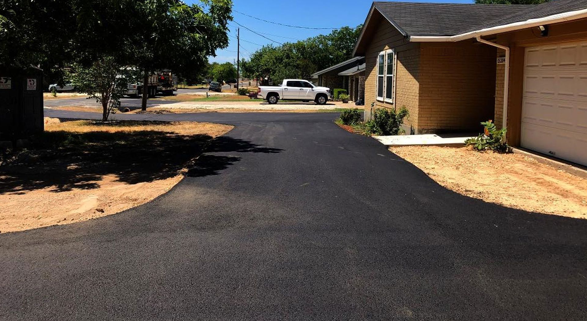 Asphalt driveway with a light-colored edge, splitting into two paths toward a house with trees in the background.