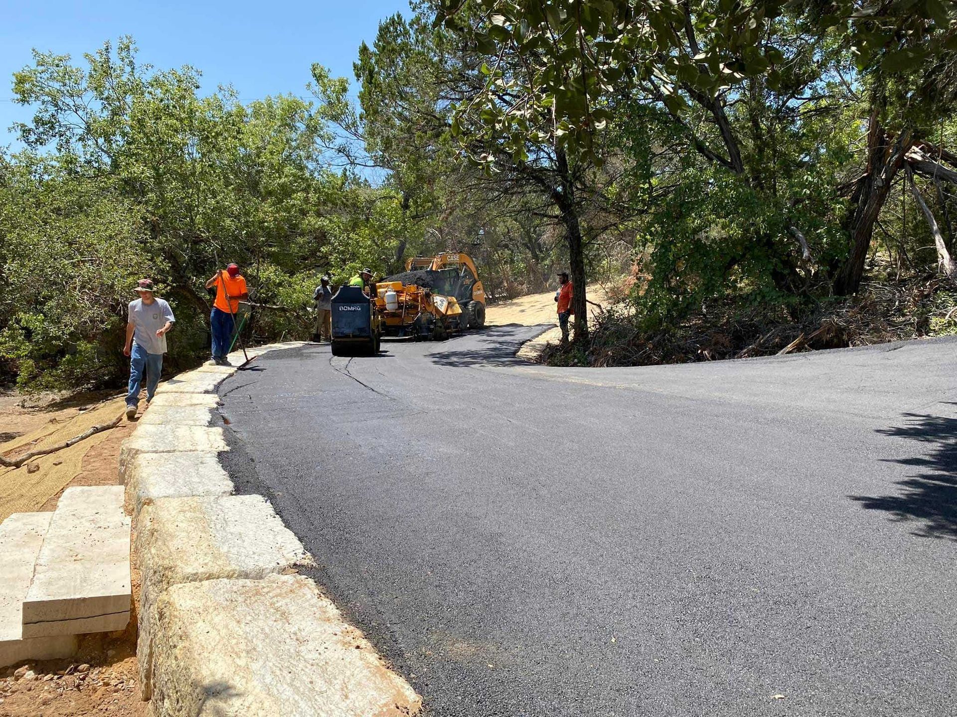 Road paving with workers and equipment on a sunny day.