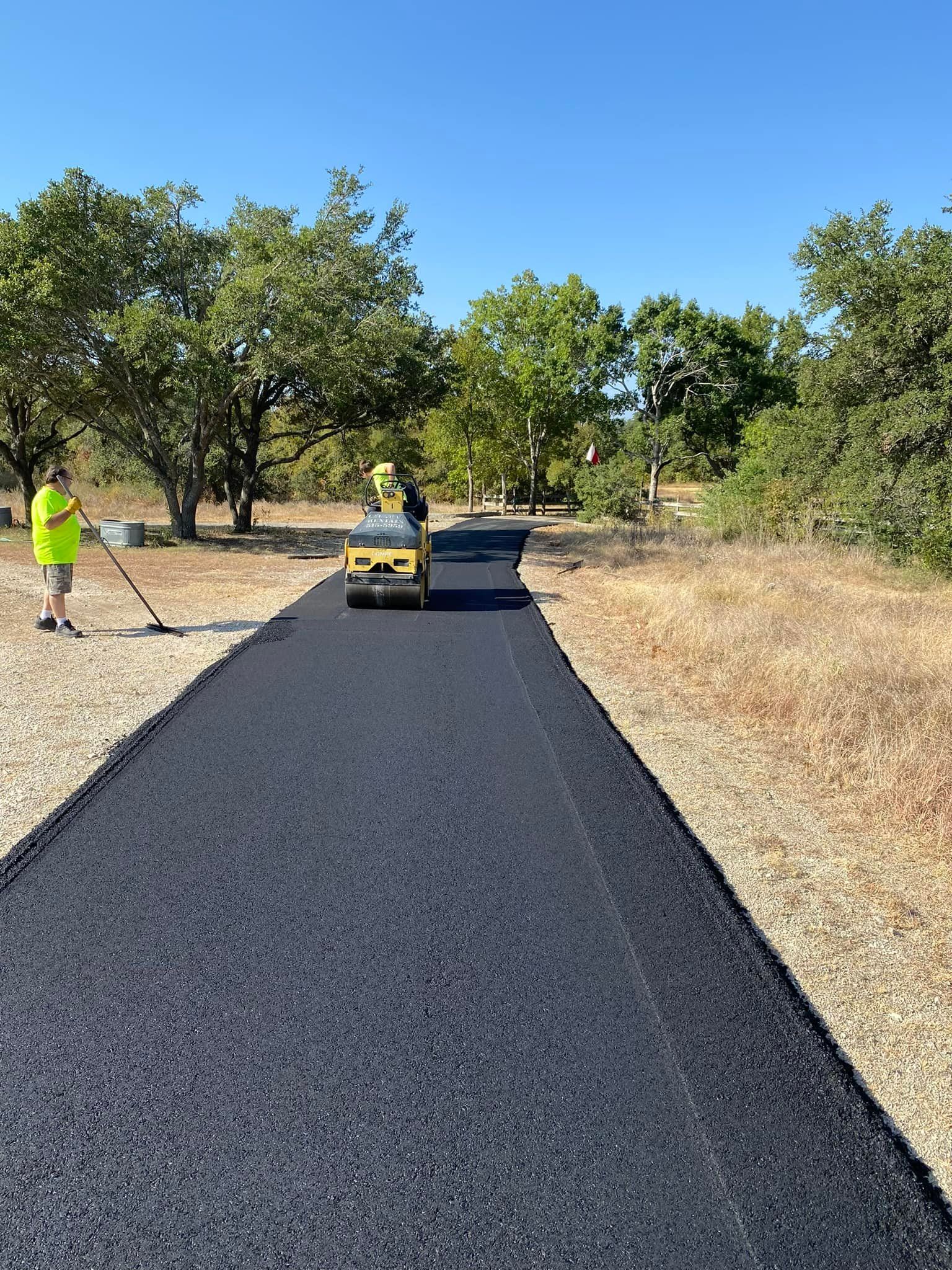 Asphalt paving of a path in a park. Workers using a roller and rake. Bright sunny day.