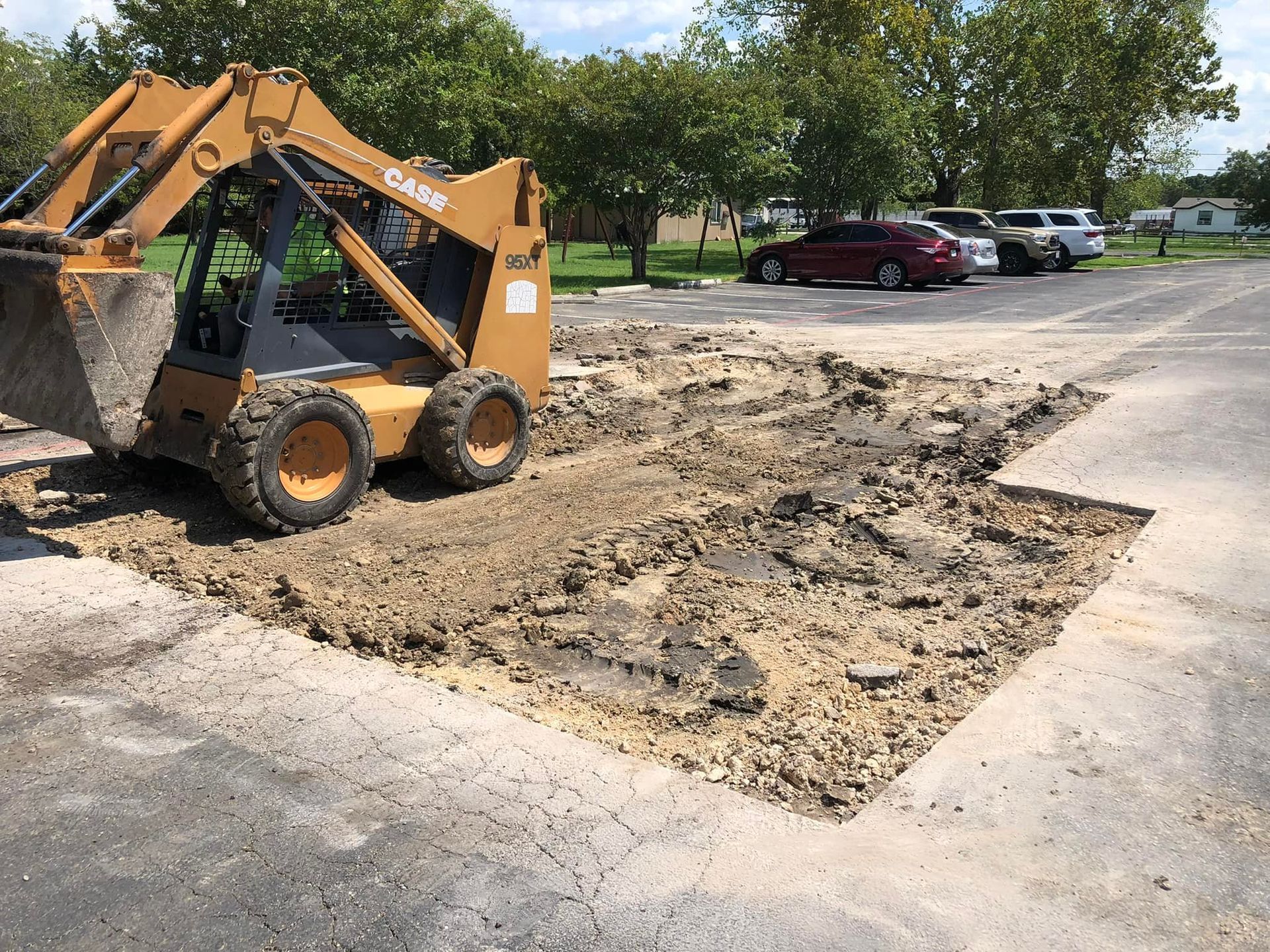 Skid steer removing asphalt in a parking lot, preparing the area for repair.