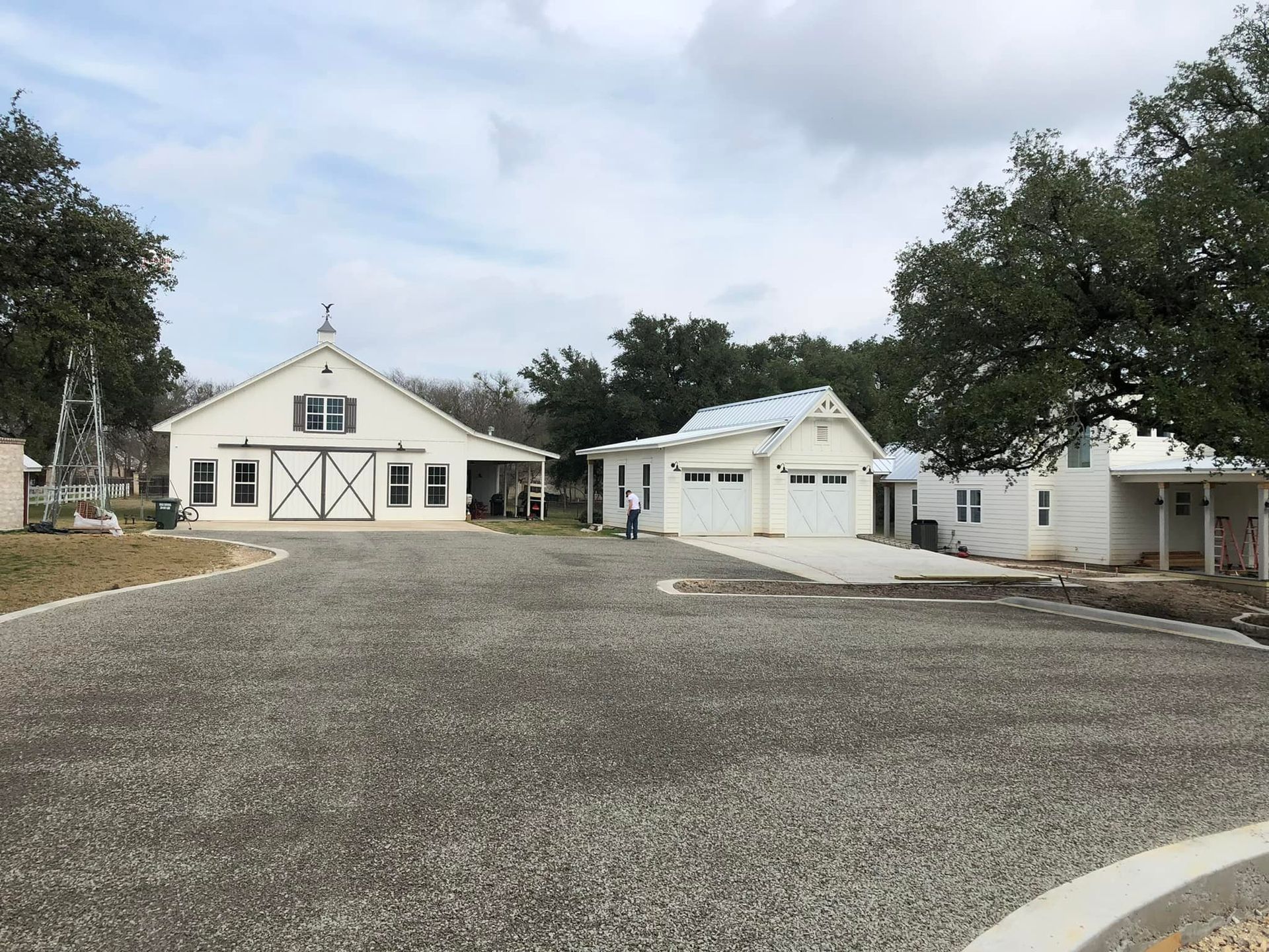 White barn and outbuildings with a gravel driveway and trees.