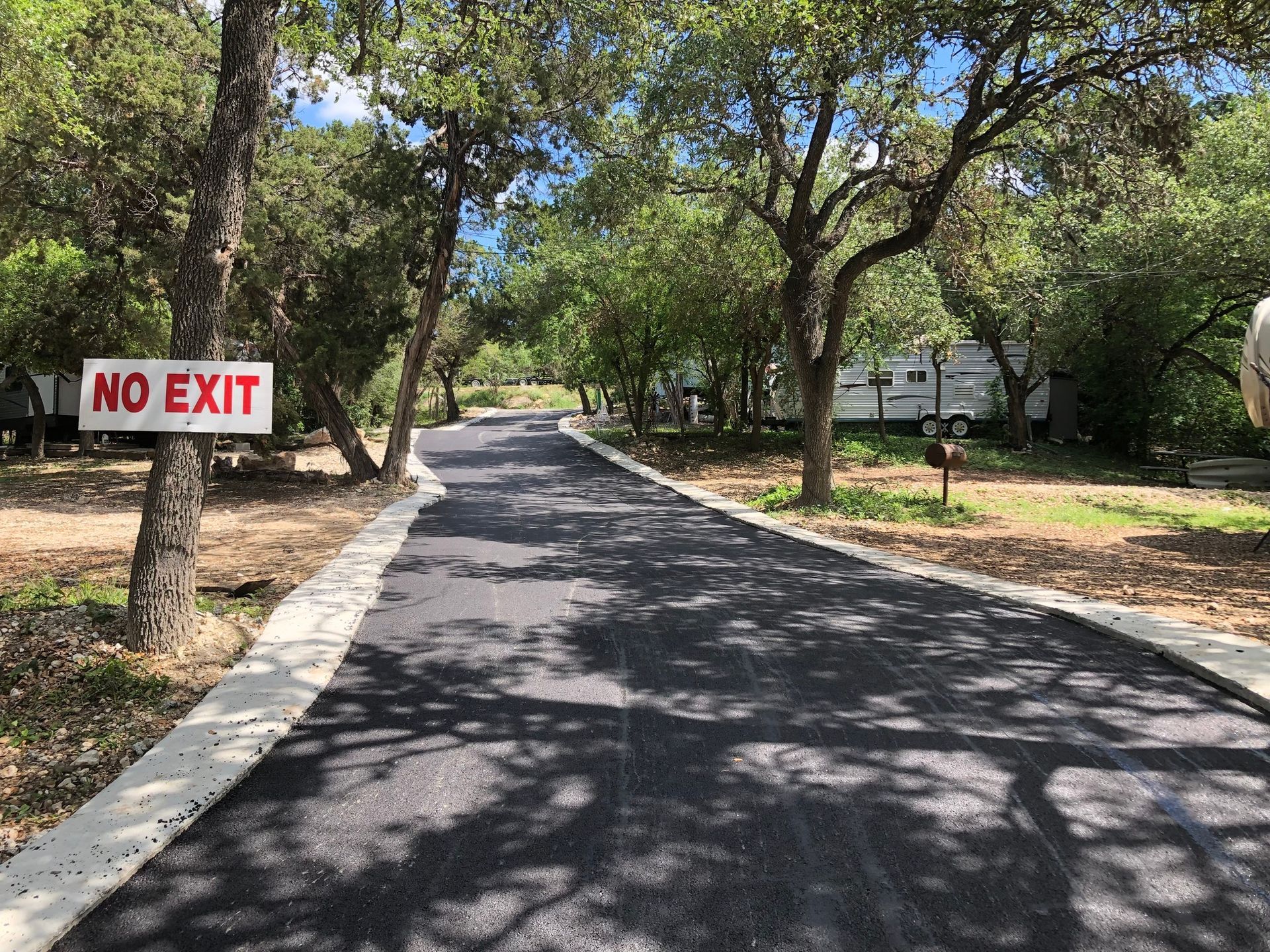 Asphalt road in a camping area with trees and RVs, a