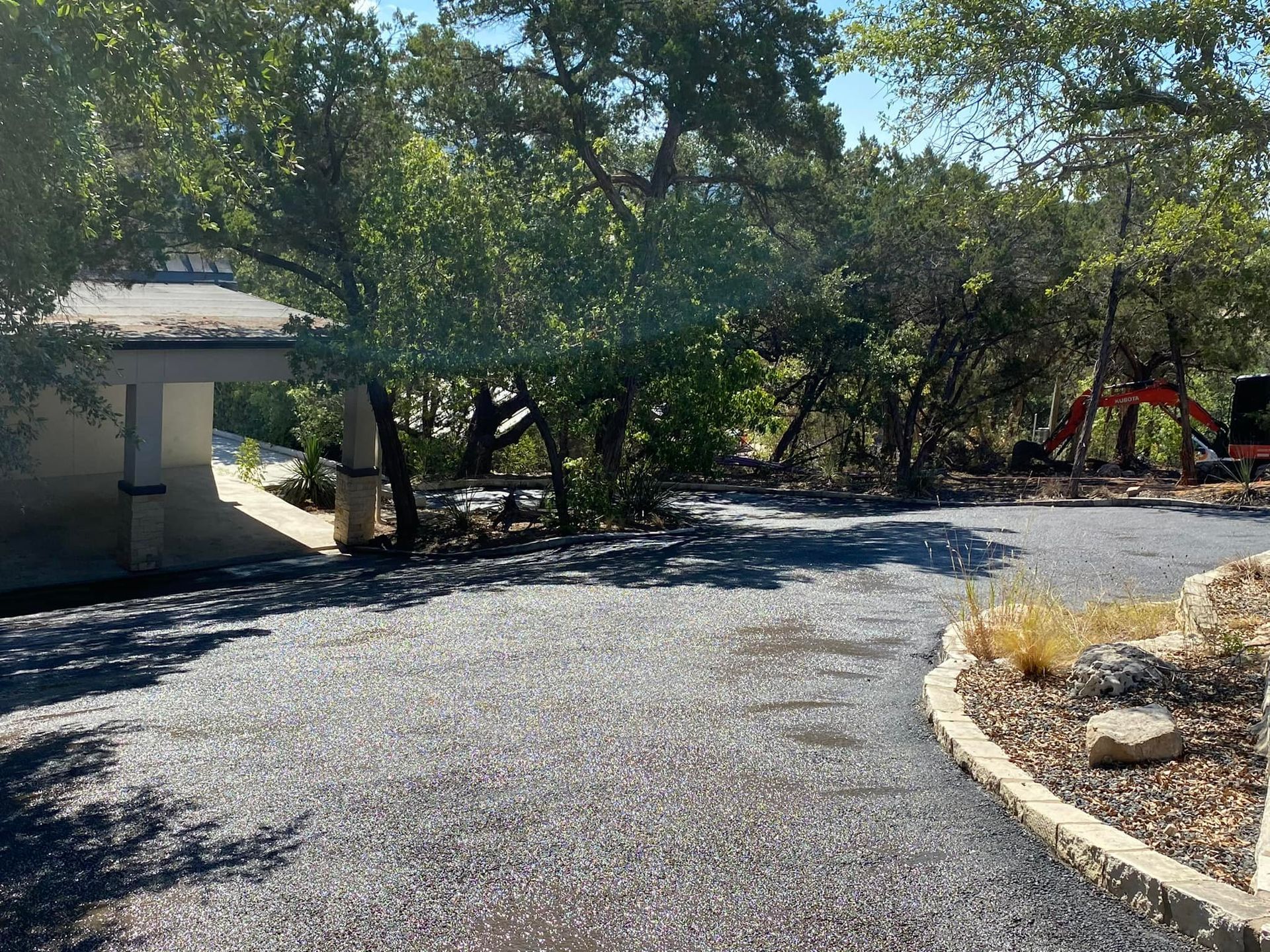 Gravel driveway curves towards a building, surrounded by trees under a sunny sky.